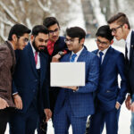 Group of six indian businessman in suits posed outdoor in winter day at Europe, looking on laptop.